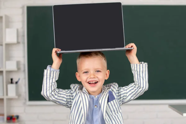 Egy kisdiák fiú laptopot tart a fején az osztályban.. — Stock Fotó