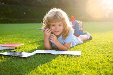 Yaz günbatımında deftere kalem yazan küçük çocuk. Yaz tatili ödevi. Anaokulu öğrencisi dışarıda..
