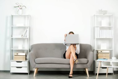 Genç çekici seksi sekreter ofiste. Güzel sekreter bacakları. Dizüstü bilgisayarı ve seksi bacakları olan baştan çıkarıcı seksi sekreter ofiste koltukta oturuyor. Şehvetli genç kız çalışan..