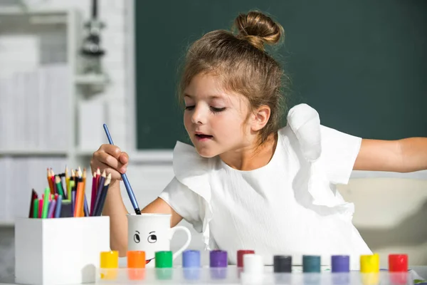 Çocuk kız sınıfta resim çiziyor, masada oturuyor, okulun karatahta arka planında eğleniyor. Erken eğitim. — Stok fotoğraf