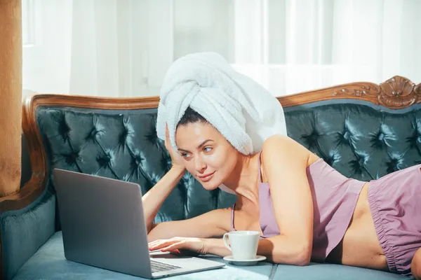 Distanza di lavoro online dal letto. Giovane donna attraente con caffè e laptop rilassante a casa. Accogliente pigro mattinata. Bella ragazza online chatta al mattino sul letto. — Foto Stock