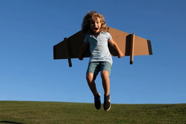 芝生の夏の丘の外の空の背景におもちゃの飛行機で遊んでいる白人の子供。幸せな未来のコンセプトを夢見て. — ストック写真