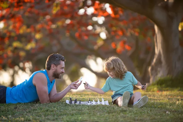 Dítě syn ležel na trávě a hrál šachy s otcem. — Stock fotografie