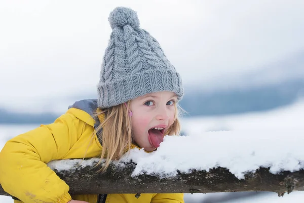 冬の女の子は屋外で雪を食べる。面白いクリスマスの子供の休日。風邪やインフルエンザの概念。舌で雪を舐めなさい。雪の日に暖かい冬服を着ている子供たち。面白い子供たちが. — ストック写真