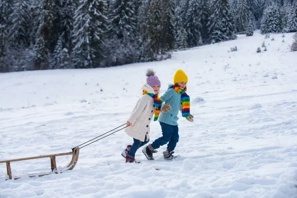 Boy and girl kids sliding with sledge in the snow. Active winter children outdoors. Snow background, copy space. — Stock Photo, Image