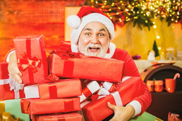 クリスマスの贈り物で興奮したシニアサンタ。サンタクロースとクリスマスグリーティングカード。白いひげを生やした祖父はクリスマスの背景にポーズをとって. — ストック写真