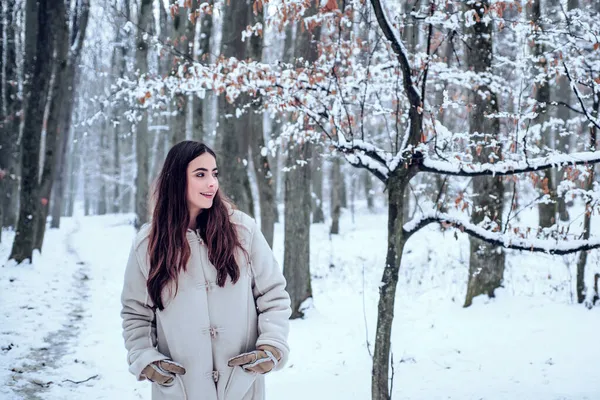 Donna invernale. Ritratto di una giovane donna sulla neve che cerca di scaldarsi. Bella ragazza nella foresta invernale in piumino bianco. — Foto Stock