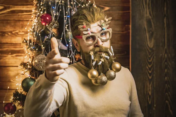 Бородатый мужчина указывает пальцем на то, что ты веселишься возле рождественской елки в помещении. Захватывающее лицо Санты вблизи. Смешной изумленный человек празднует Рождество. — стоковое фото