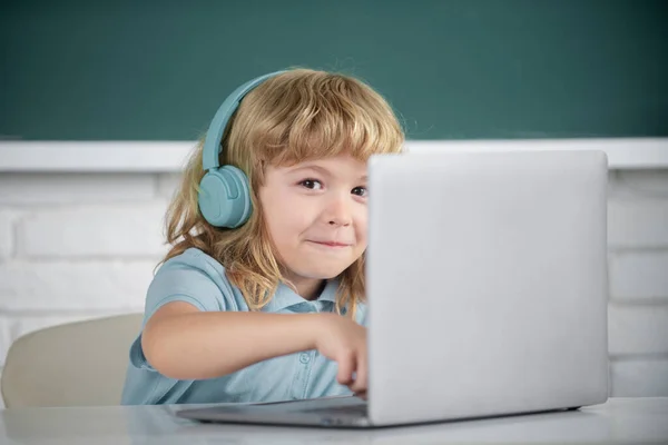 Close up retrato de menino pequeno em fones de ouvido assistir vídeo lição no computador na escola, criança em fones de ouvido têm aula on-line, usando laptop. — Fotografia de Stock