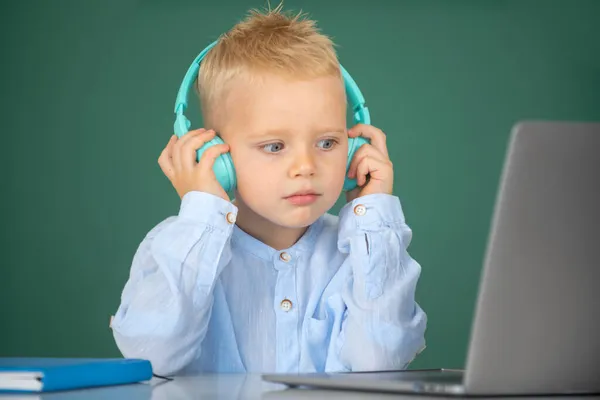Niño pequeño en los auriculares ver video lección en la computadora en la escuela, niño en los auriculares tienen lección en línea, utilizando el ordenador portátil. Formación informática. — Foto de Stock