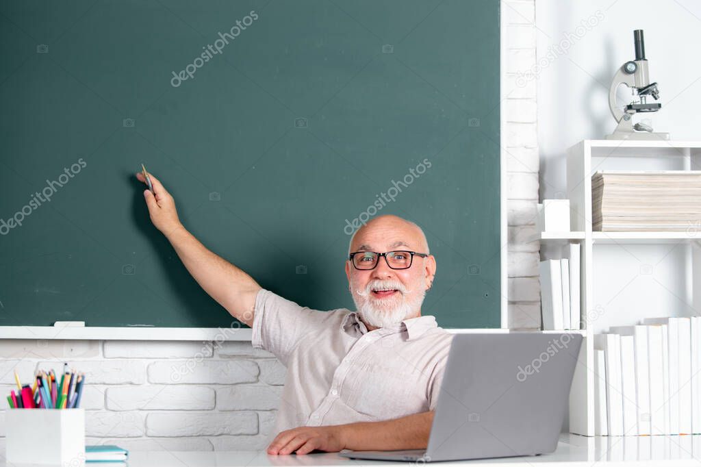 Portrait of senior teacher teaching line of high school students with computer laptop in classroom.