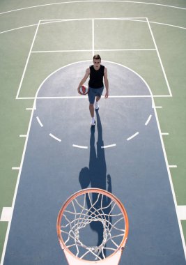 Basketbolcu, tişörtlü ve şortlu sporcu, basketbol topunu şehir arka planında tutuyor. Spor motivasyonu kavramı.