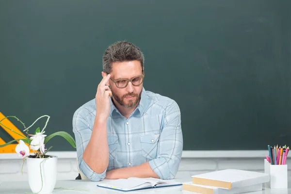 Portret van denkende leraar of docent professor die aan tafel werkt op de universiteit of middelbare school. Jonge moderne mannelijke leraar wachtend op studenten. — Stockfoto