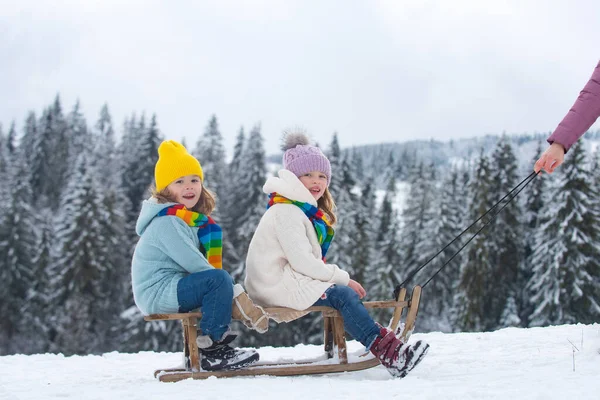 Αγόρι και κορίτσι κάνουν έλκηθρο σε ένα χιονισμένο δάσος. Υπαίθρια παιδιά χειμώνα διασκέδαση για τα Χριστούγεννα και την Πρωτοχρονιά. Παιδιά απολαμβάνουν μια βόλτα με έλκηθρο. Οικογενειακές διακοπές Χριστούγεννα υπαίθρια. — Φωτογραφία Αρχείου