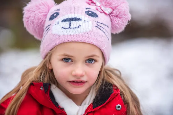 Ritratto ravvicinato di bella ragazza bionda che gioca nel cappello caldo invernale su uno sfondo di neve. Carino faccia bambini. — Foto Stock