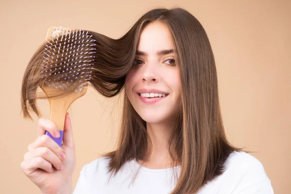 Portrait of beautiful young woman combing her hair, smiling. Female brushing healthy hair with comb. — Stock Photo, Image