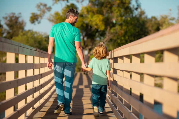 Achteraanzicht van vader en zoon wandelen op houten brug buiten, Vaderdag concept. — Stockfoto