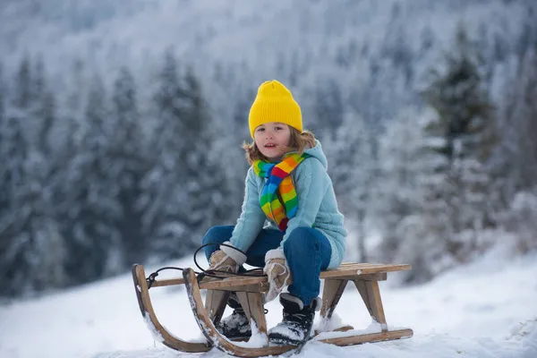 Kluk na saních, užívající si jízdu na saních. Dítě sedí na saních. Děti si hrají se sněhem na zimním pozadí sněhu a mrazu. Koncept zimní dovolené. — Stock fotografie