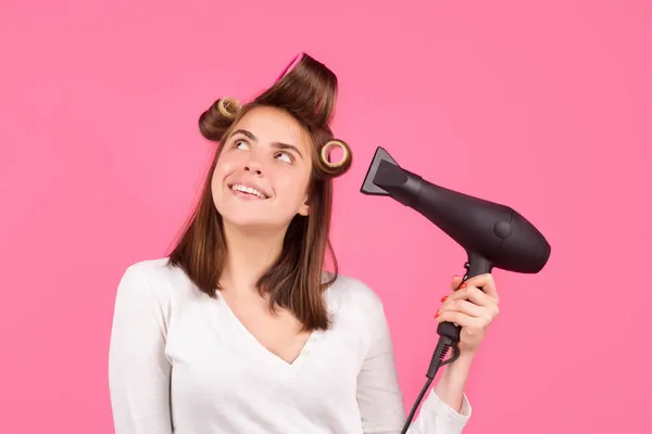 Smiling woman with hair dryer and rollers. Woman with hair dryer. Beautiful girl with straight hair drying hair with professional hairdryer.
