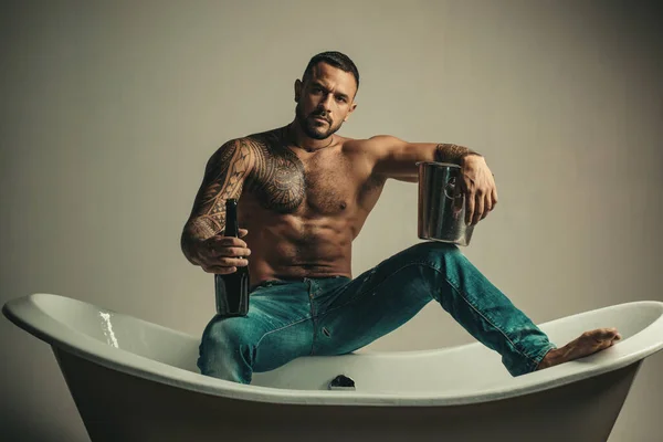 Sexy homme musclé séduisant assis sur la baignoire, les hommes vacances avec du champagne. Célébrer Noël ou anniversaire. Partie de sexe privé. — Photo