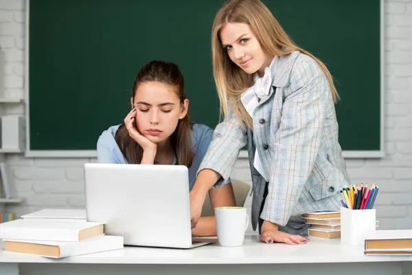 Studenter flickor vänner i klassrummet på skolan college eller universitet på svarta tavlan bakgrund. Två studenter tittar på bärbar dator gör läxor tillsammans och hjälpa varandra. — Stockfoto