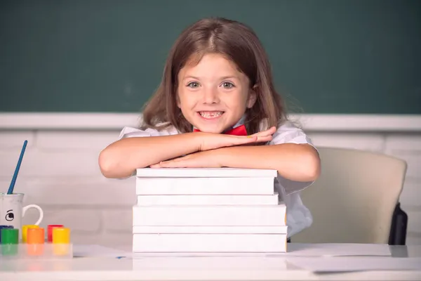 Ragazza sorridente seduta alla scrivania e che tiene per mano i libri in classe. Processo educativo. — Foto Stock