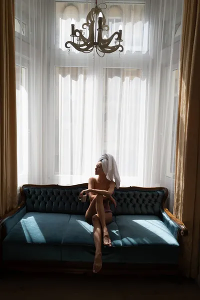 Κορίτσι αναπαύεται και ξαπλώνει σε άνετο καναπέ-κρεβάτι στην πολυτελή κρεβατοκάμαρα ένα εύκολο πρωινό. Ελκυστική σέξι γυναίκα χαλαρώνοντας στο δωμάτιο του ξενοδοχείου, φορώντας μπουρνούζια και πετσέτες, πίνοντας καφέ. — Φωτογραφία Αρχείου