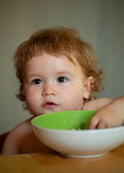 Bébé drôle manger de la nourriture lui-même avec une cuillère sur la cuisine. — Photo