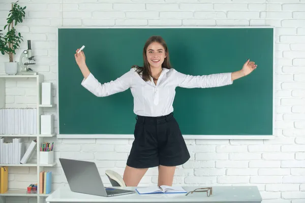 Estudiante emocionada estudiante amazet con las manos levantadas sosteniendo tiza en la escuela secundaria o la universidad en el fondo de pizarra. — Foto de Stock