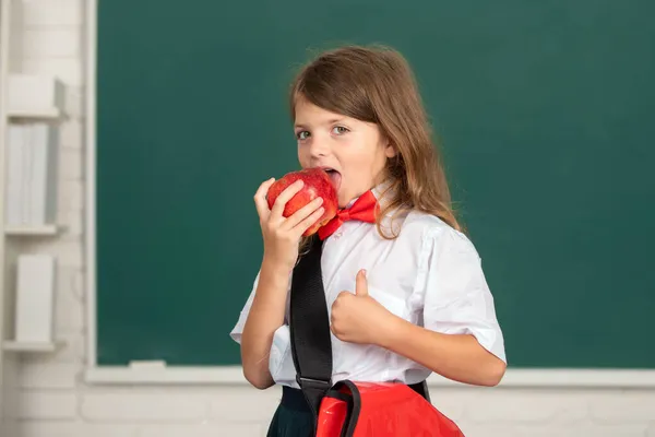 Porträt eines hübschen Mädchens mit rotem Apfel im Klassenzimmer. Geniales Kind, Wissenstag. — Stockfoto
