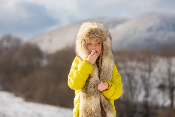 Αστείο κοριτσάκι που περπατάει τρώγοντας χιόνι τη χειμωνιάτικη μέρα. Συναρπαστικές γιορτές. Παιδιά κρύο και γρίπη έννοια. — Φωτογραφία Αρχείου