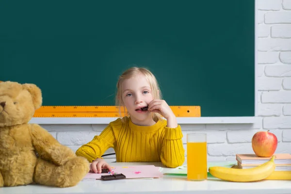Маленька школярка їсть шоколад на уроках, вивчає англійську мову в школі. Геніальна дитина, день знань. Діти освіта та знання . — стокове фото
