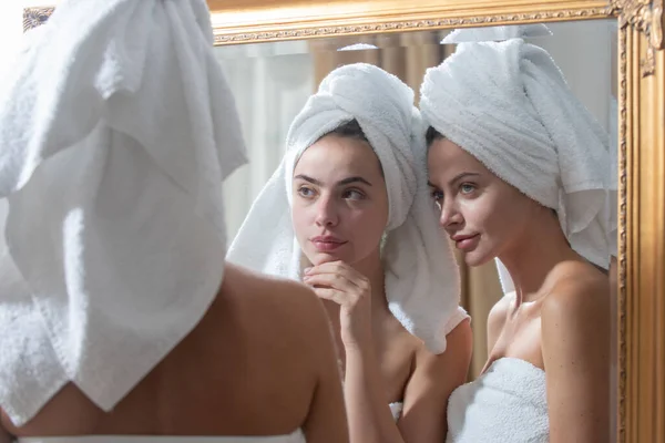 Bella donna si guarda allo specchio dopo la doccia in appartamento o in camera d'albergo. Giovani belle ragazze amici avvolti in asciugamano levigatura perfezionare la pelle, concetto di routine quotidiana mattina. — Foto Stock