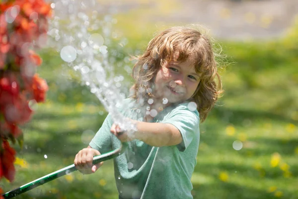 Счастливый маленький мальчик веселится в саду. Дети держат поливающий садовый шланг. Активные игры на открытом воздухе для детей на заднем дворе во время сбора урожая — стоковое фото