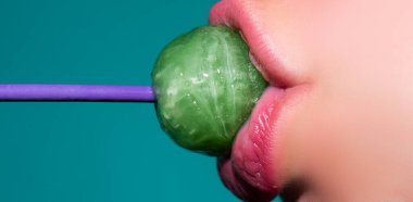 Ağzında lolipop var, yakın plan. Ağzında lolipop olan güzel bir kız. Parlak kırmızı kadın dudakları. Ağız yalamak chupa chup emmek.