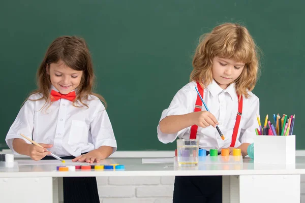 Los niños de la escuela dibujan dibujos coloridos con lápices de colores en el aula sobre fondo de pizarra. Retrato de alumnos lindos disfrutando de clases de arte y artesanía. —  Fotos de Stock