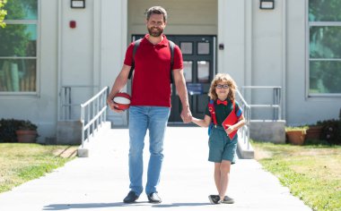 Baba oğluna okula kadar eşlik ediyor. Sırt çantalı ilkokul öğrencisinin ebeveyni ve öğrencisi..