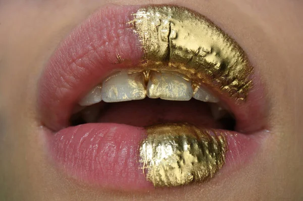 Gold lips. Gold paint from the mouth. Golden lips on woman open sensual mouth with make-up. Sensual and creative design for golden metallic.