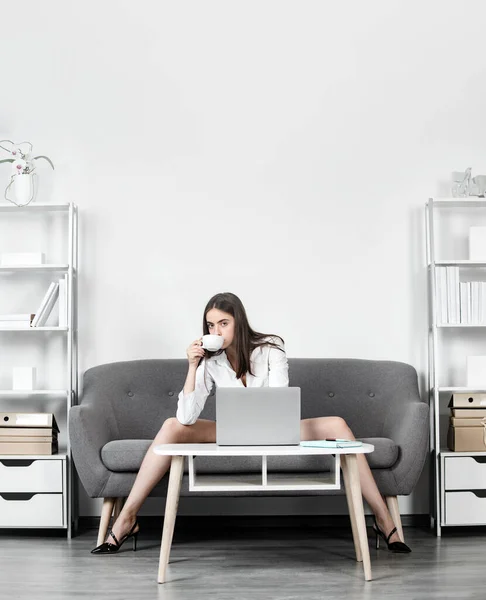 Verführerische Sekretärin mit sexy Beinen, Kaffee trinkend, auf dem Sofa im Büro sitzend. Sexy Geschäftsfrau. Sinnliche Mädchen Mitarbeiter. — Stockfoto