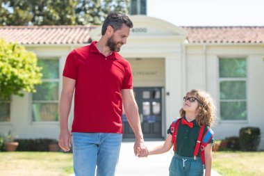 Baba oğluna okula kadar eşlik ediyor. Sırt çantalı ilkokul öğrencisinin ebeveyni ve öğrencisi..