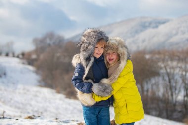 Kışın dışarıda kucaklaşan komik çocuklar. Dışarıda karlı bir günde gülümseyen çocuklar. İki çocuk birlikte parkta kar geçmişi olan bir kız. Mutlu çocuk duyguları..
