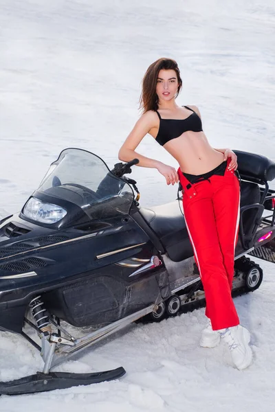 Mujer sexy posando con moto de nieve en invierno nevado. Nieve chica móvil de conducción. Diversión de invierno. — Foto de Stock