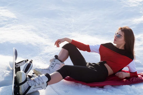 Woman snowboarder relax on snow. Sexy woman with snowboard in winter. Woman snowboarder rest. Skiing snow board, winter season.