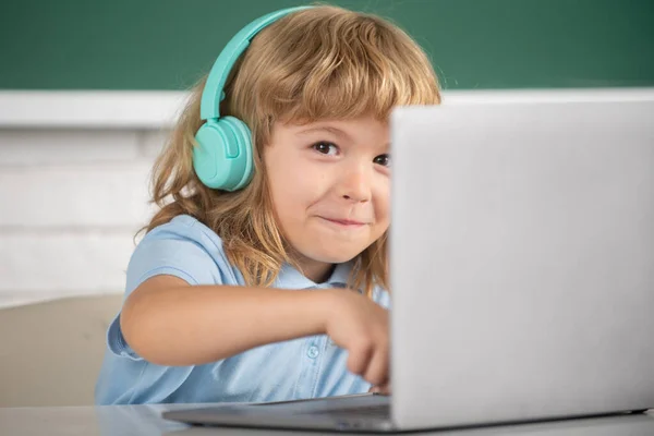 Primer plano retrato de niño lindo en auriculares usando un ordenador portátil y estudiar en línea con el profesor de videollamada en la escuela. — Foto de Stock