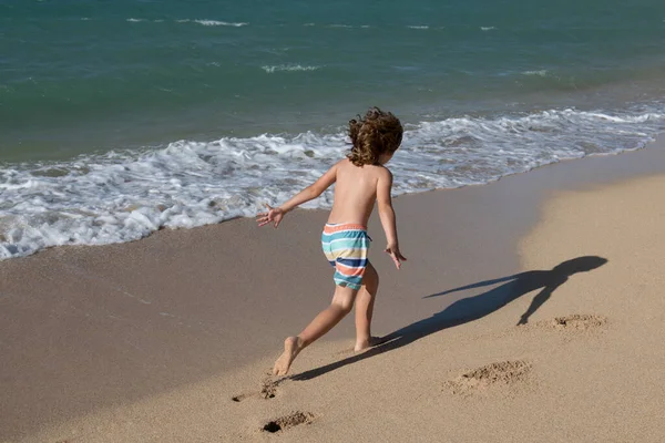 少年は夏休みにビーチで遊ぶ。海の水の中を走る美しい海と砂と青の自然の中の子供たち. — ストック写真