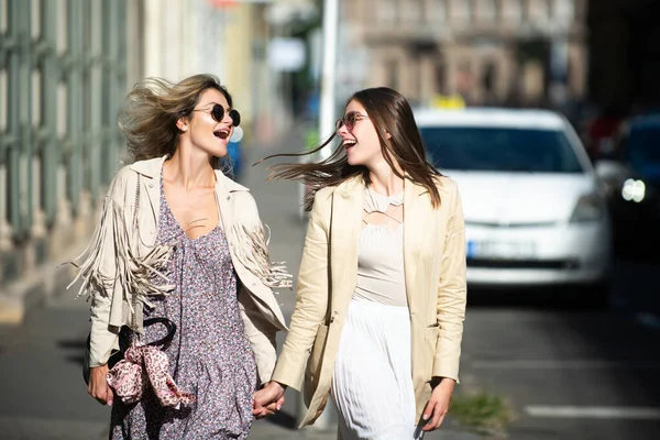 Dos jóvenes lanzadoras con gafas de sol caminando por la ciudad. Vacaciones divertidas, viajes románticos. —  Fotos de Stock