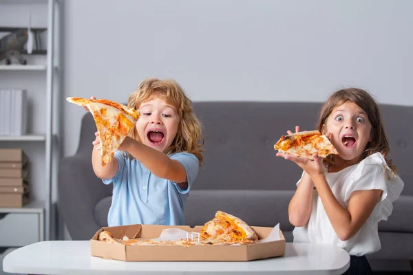 Niños comiendo pizza. Niños emocionados comiendo pizza. Dos niños pequeños muerden pizza adentro. — Foto de Stock