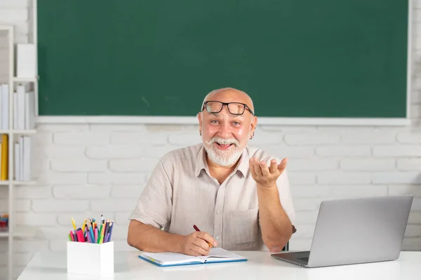 男人成熟的老师。高中或大学时，戴着眼镜、在黑板上挂着书的快乐的高中导师的画像。上大学时的老学生。成人教育. — 图库照片