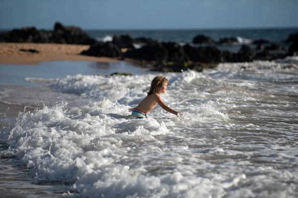 Kid Jumping in Sea Ocean Waves. Jump by Water splashes. Summer day, ocean coast, Beach. Active kids lifestyle and recreation concept.