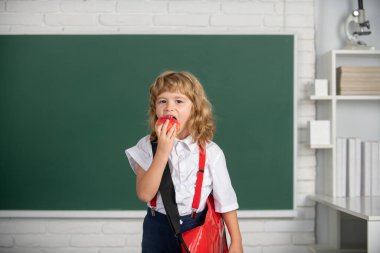 Sınıfta elma yiyen küçük bir öğrenci, okulda İngilizce öğreniyor. Dahi çocuk, bilgi günü.